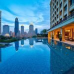 Luxury hotel infinity pool overlooking city skyline at dusk.