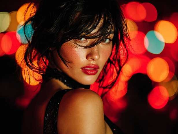 Glamorous woman with red lipstick and flushed cheeks, posing against a bokeh background.