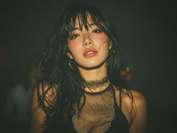 Sensual Asian woman with dark hair and a lace top, posing in a dimly lit setting.