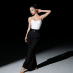 Elegant woman in white corset and black pants poses gracefully in studio lighting.