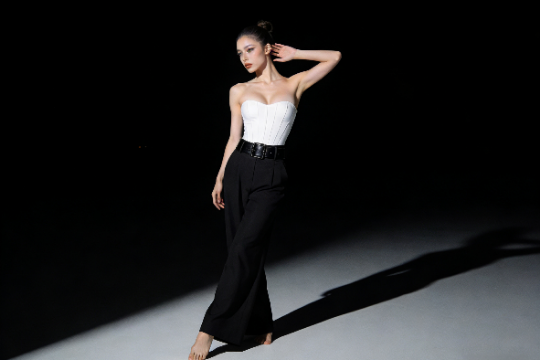 Elegant woman in white corset and black pants poses gracefully in studio lighting.