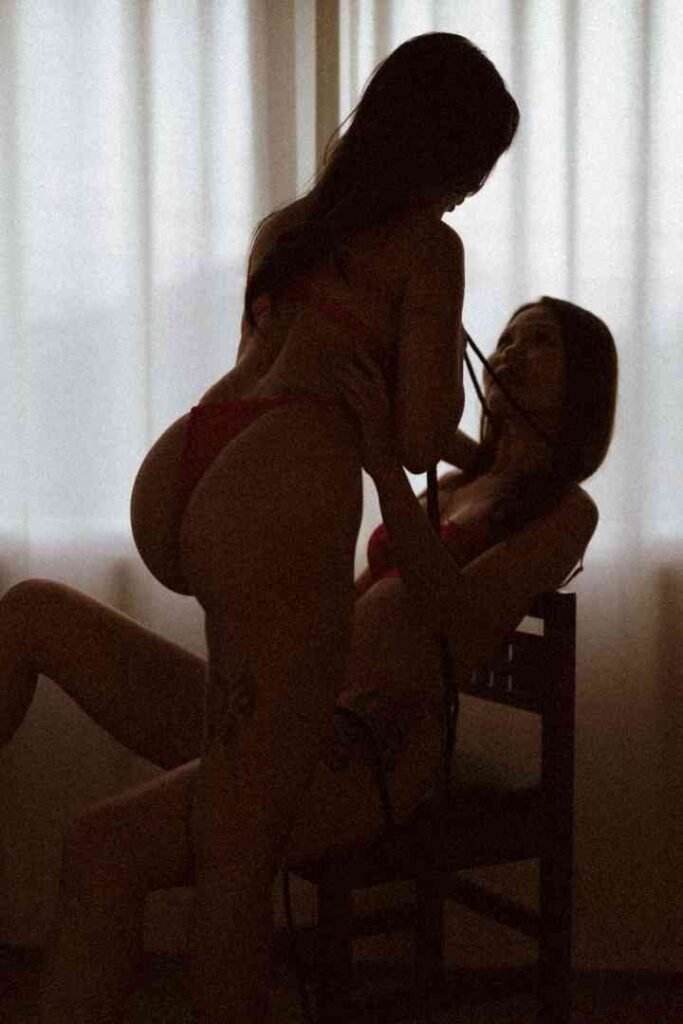Two women in red bikinis, one sitting on chair with another woman behind her