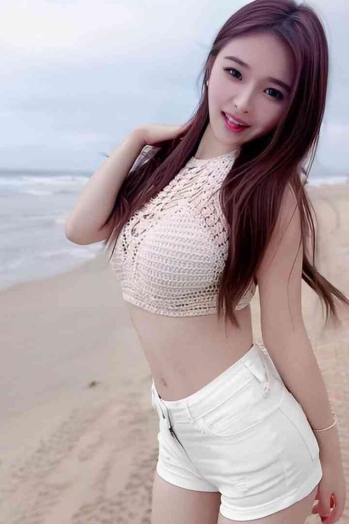 Young woman with long brown hair in a white crochet top and shorts on a beach