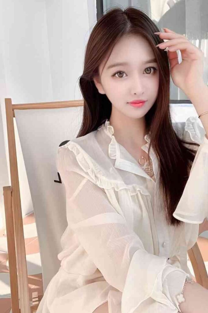 Young Taiwanese woman with long brown hair, wearing a white ruffled blouse, posing for a photo.