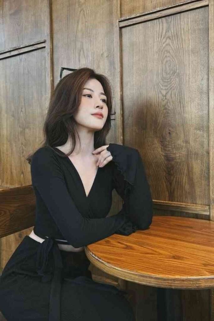 Tina, 23yo local Malay escort in KL, wearing black dress, sitting at wooden table