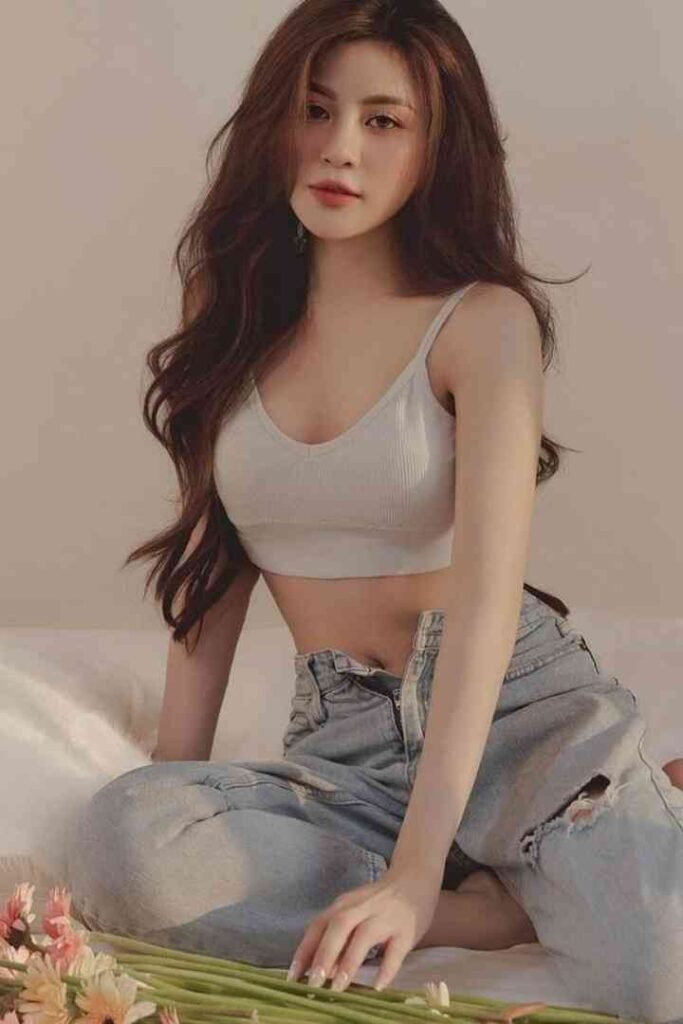 Tina, 23yo Malay escort in KL, sitting on bed with gray crop top and jeans