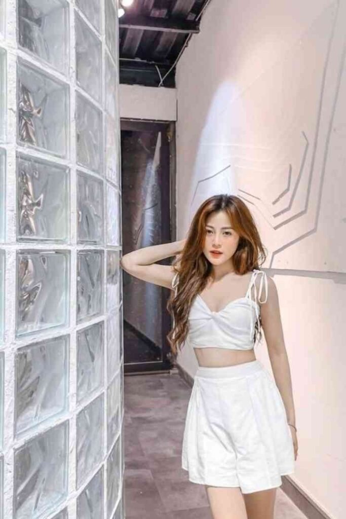 Young woman in white crop top and skirt posing indoors