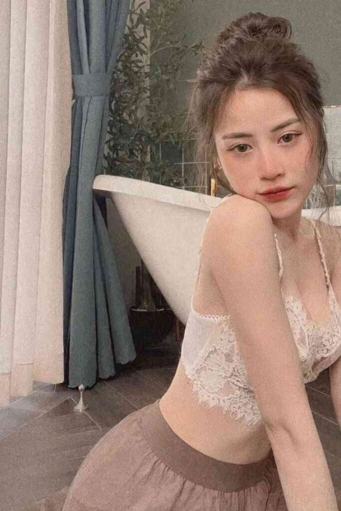 Young woman with hair up, wearing lace top and skirt, near bathtub