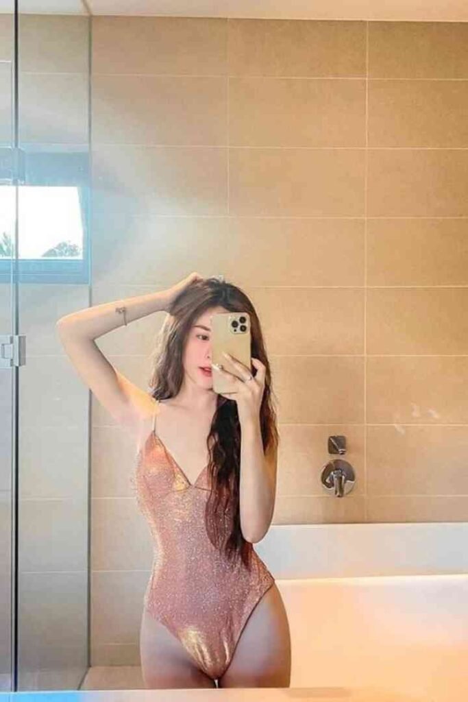 Young woman in a sparkly swimsuit poses for a mirror selfie in a bathroom.