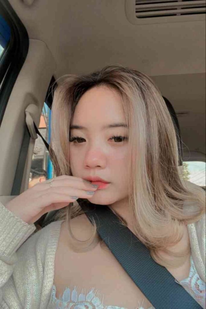 Young woman with blonde-streaked hair in a car, wearing a cardigan.
