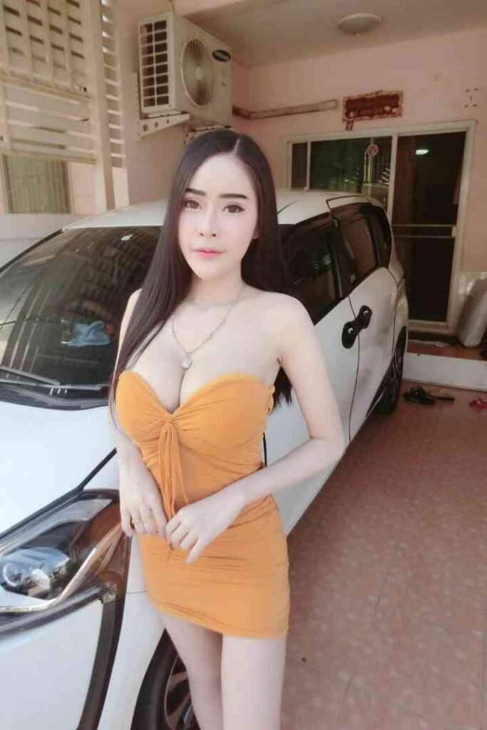 Young Thai woman in a yellow dress posing by a white car