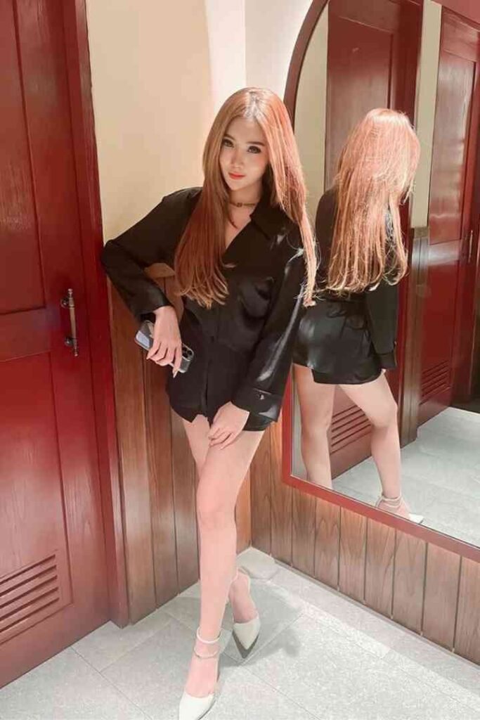 Kenzo, a 23yo local Malay escort, in a black leather dress standing in front of a mirror