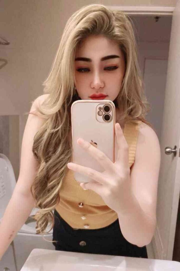 Woman with blonde hair taking selfie with iPhone in bathroom