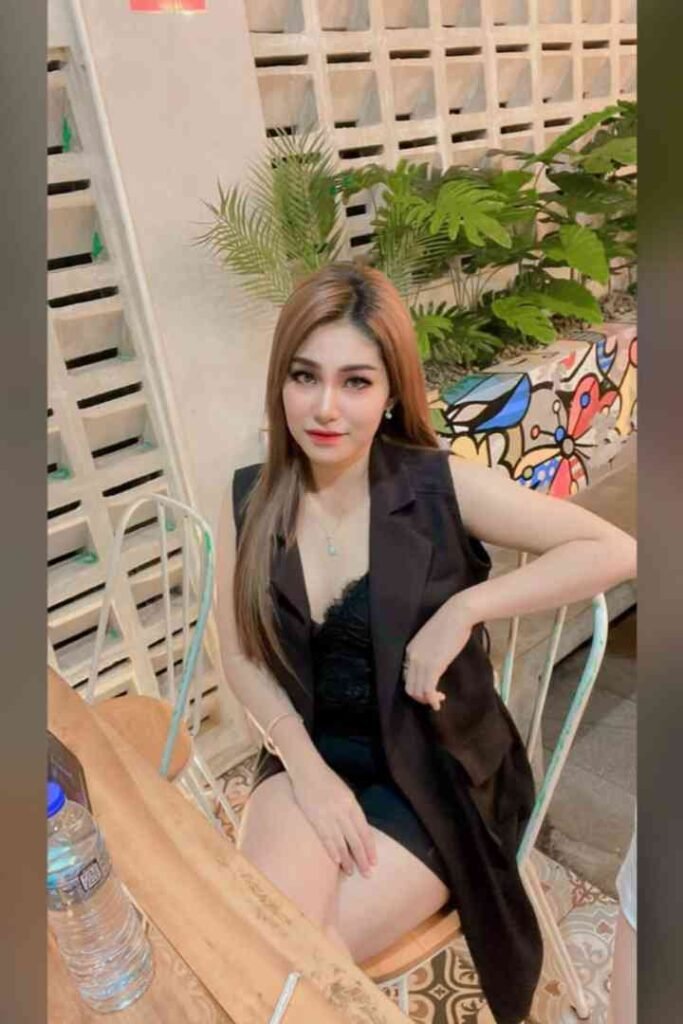 Woman in black outfit sitting on chair in outdoor cafe, smiling