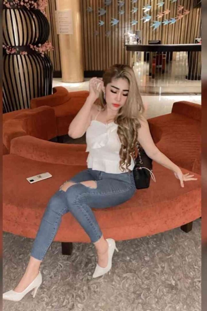 Blonde woman in white top and ripped jeans sitting on red couch with smartphone