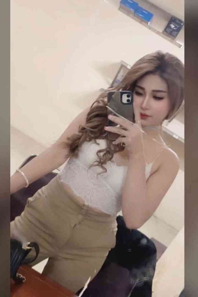 Brunette woman in white top and beige skirt taking selfie