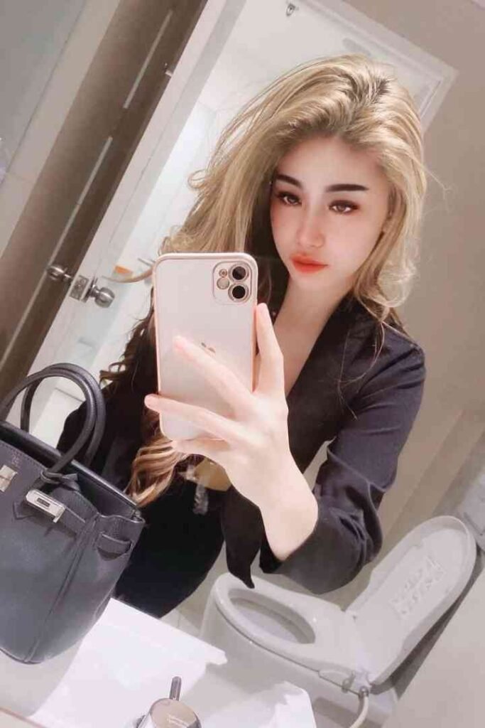 Blonde woman taking selfie in bathroom with black handbag