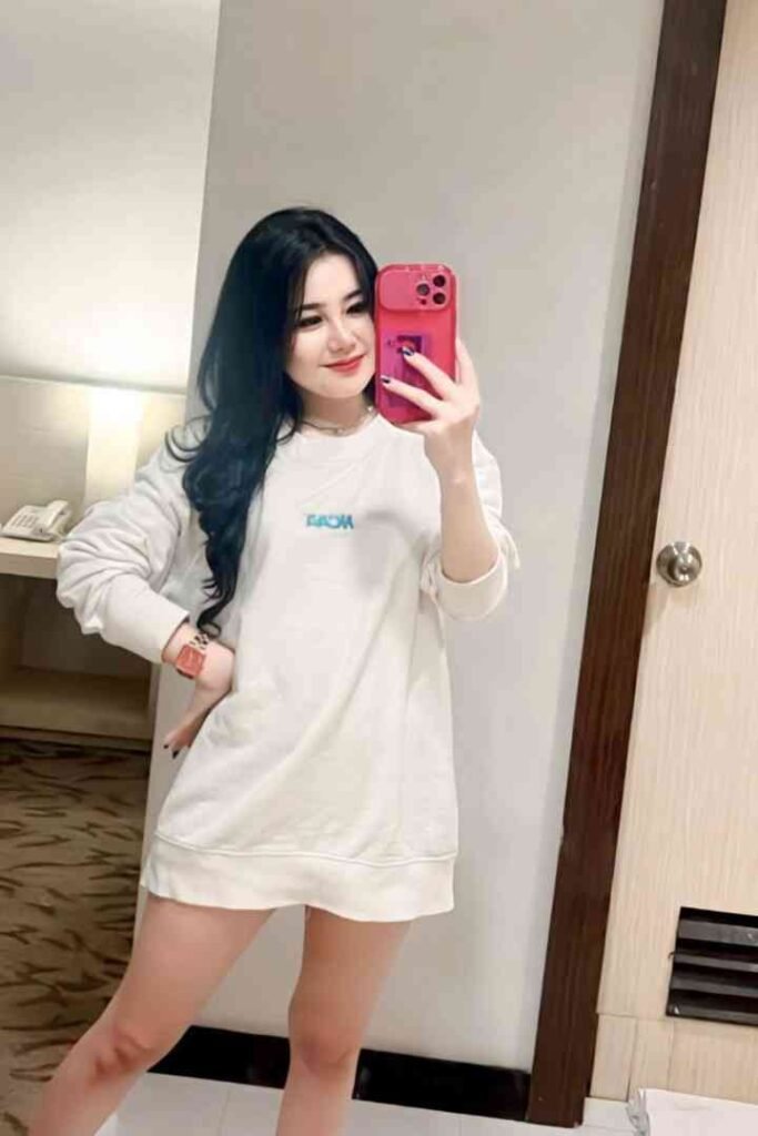 Young woman in a white sweatshirt taking a mirror selfie with a pink phone