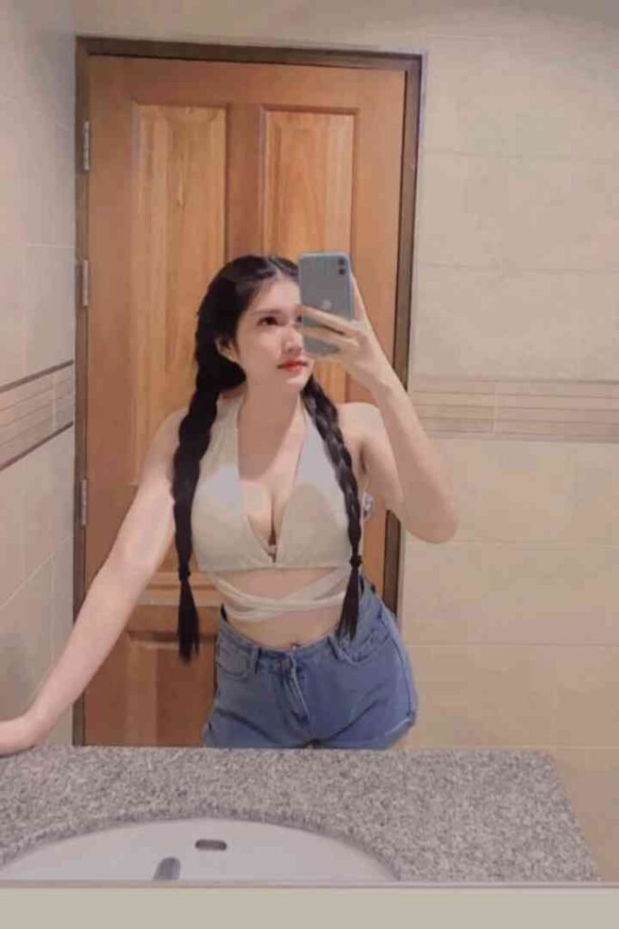 Young Thai woman with braided hair in denim shorts taking a mirror selfie.