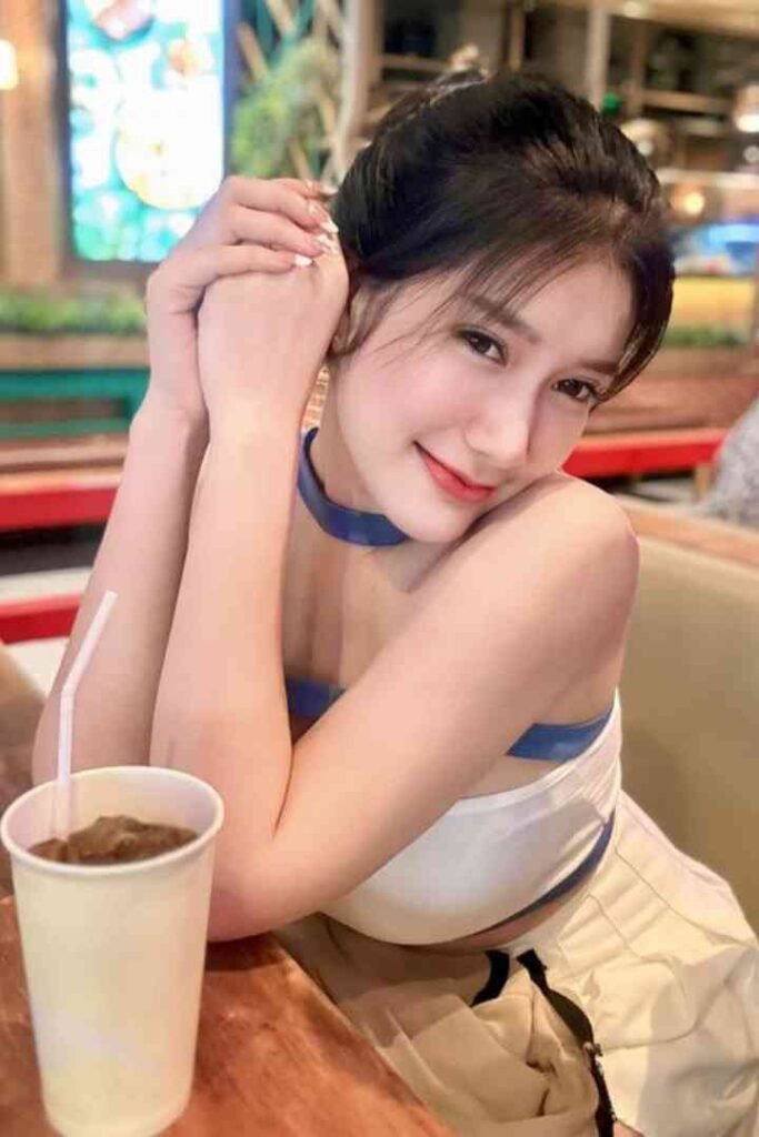 Young Thai woman with dark hair wearing a white and blue outfit, holding hands to chin