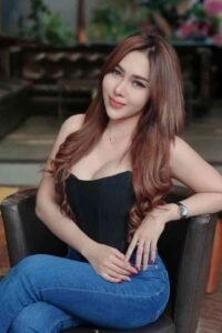 Woman with long brown hair wearing black corset and blue jeans sitting on black chair