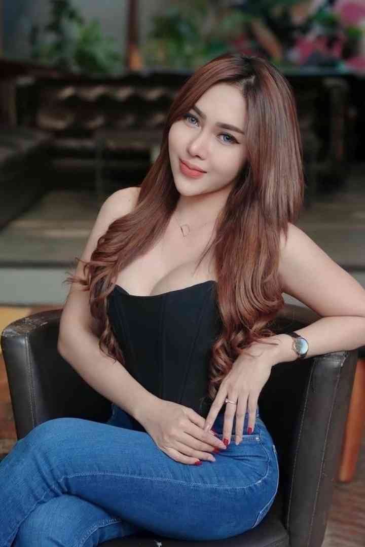 Woman with long brown hair wearing black corset and blue jeans sitting on black chair