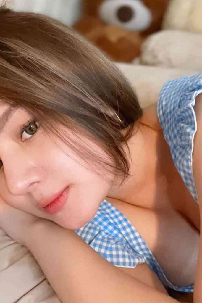 Brunette woman in blue gingham blouse lying on bed with teddy bear