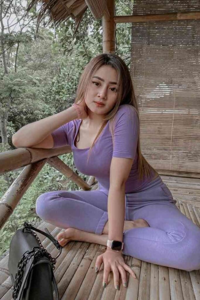 Woman in purple outfit sitting on bamboo floor with handbag