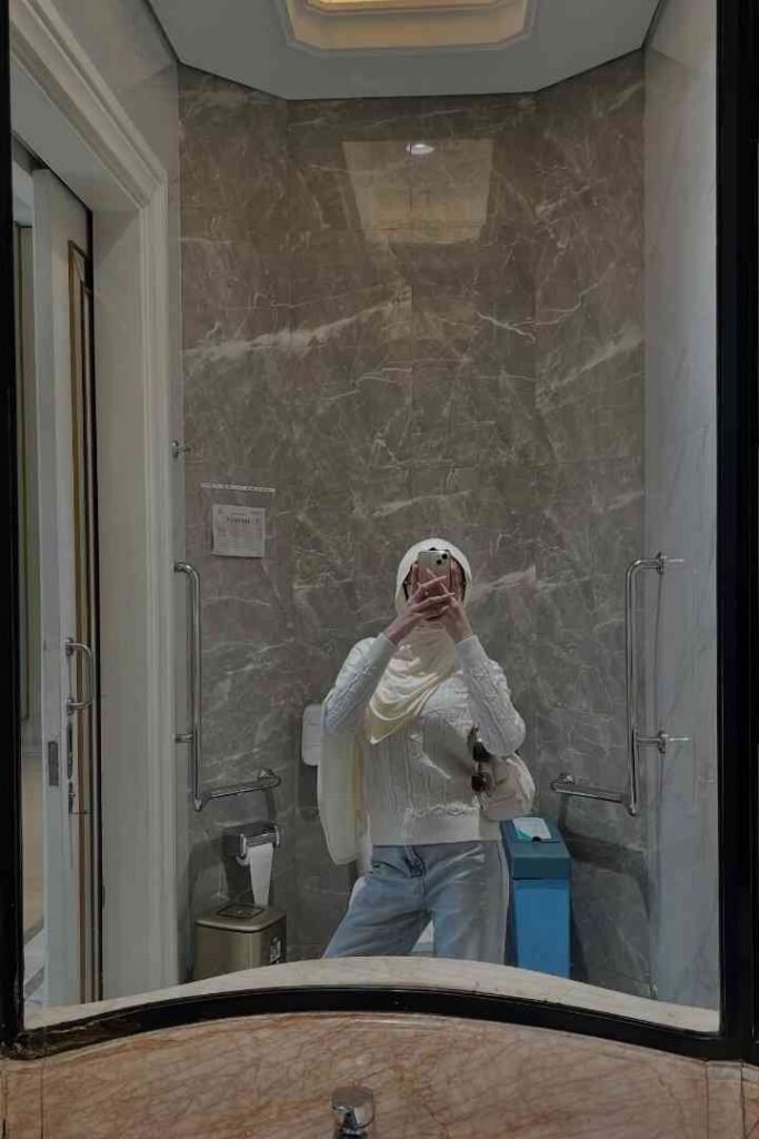 Woman in hijab taking a mirror selfie in a modern bathroom