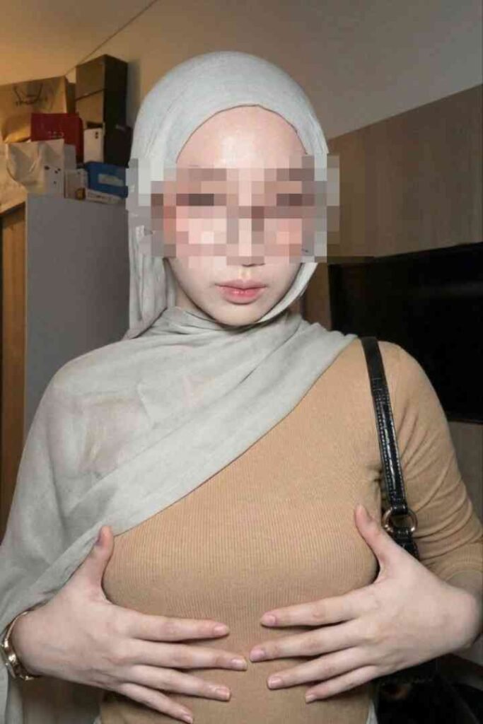 Woman in hijab and tan top, hands on chest